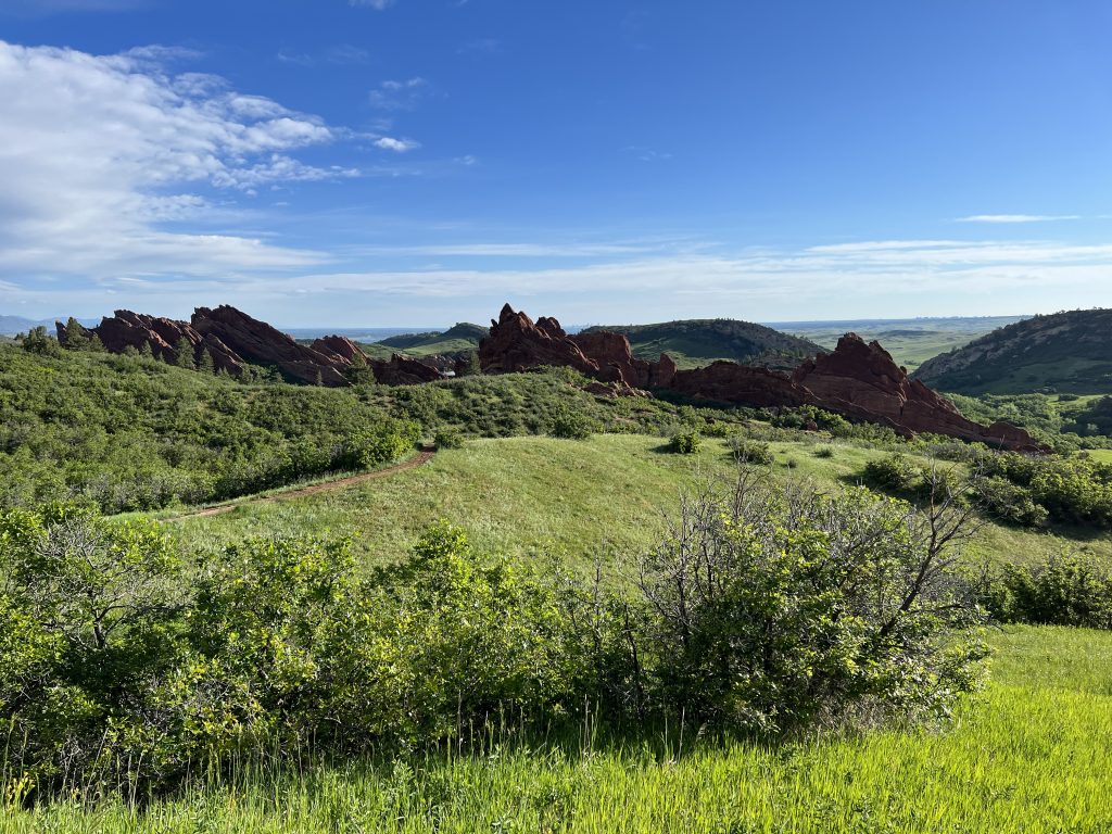 Green hills with red granite rock formations sticking out from the ground. The sky is blue and partially obscured by white clouds.