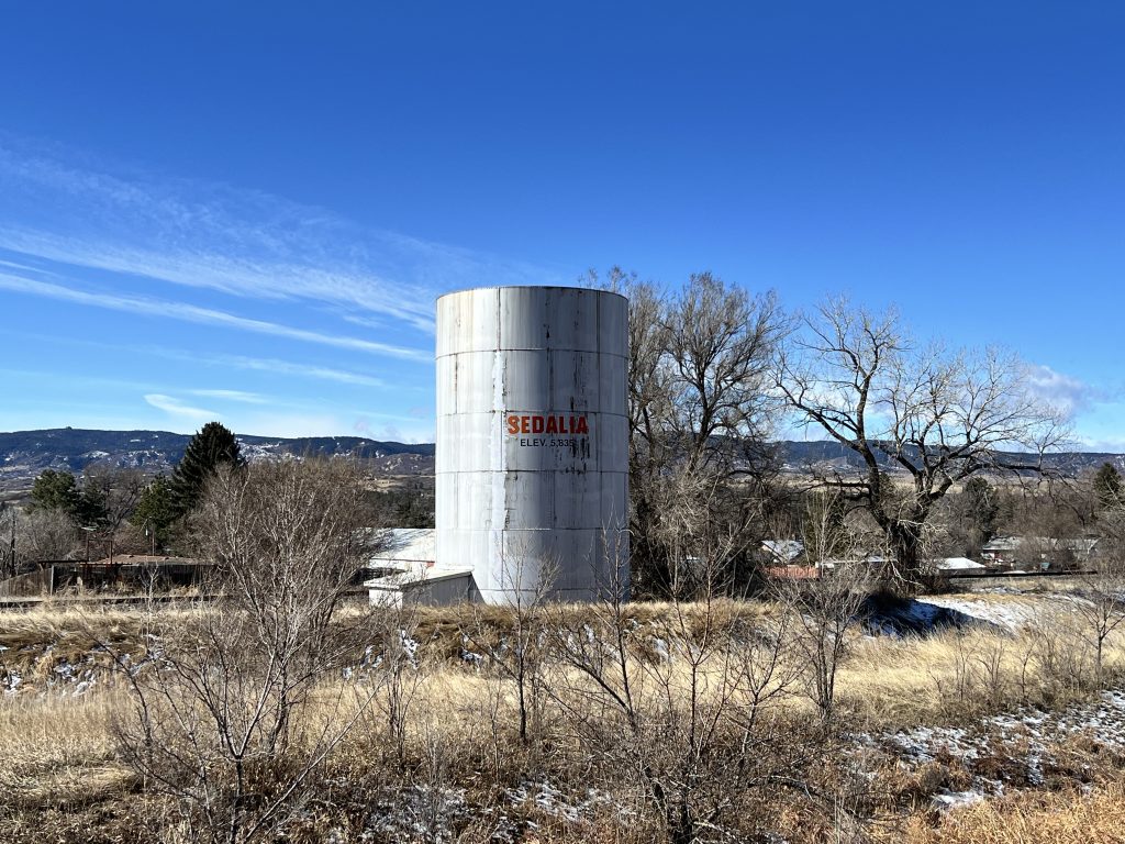 Santa Fe Railway Water Tank / Sedalia Water Tank. Photo is of a steel tank that says Sedalia, Elev. 5835 against a blue sky. 